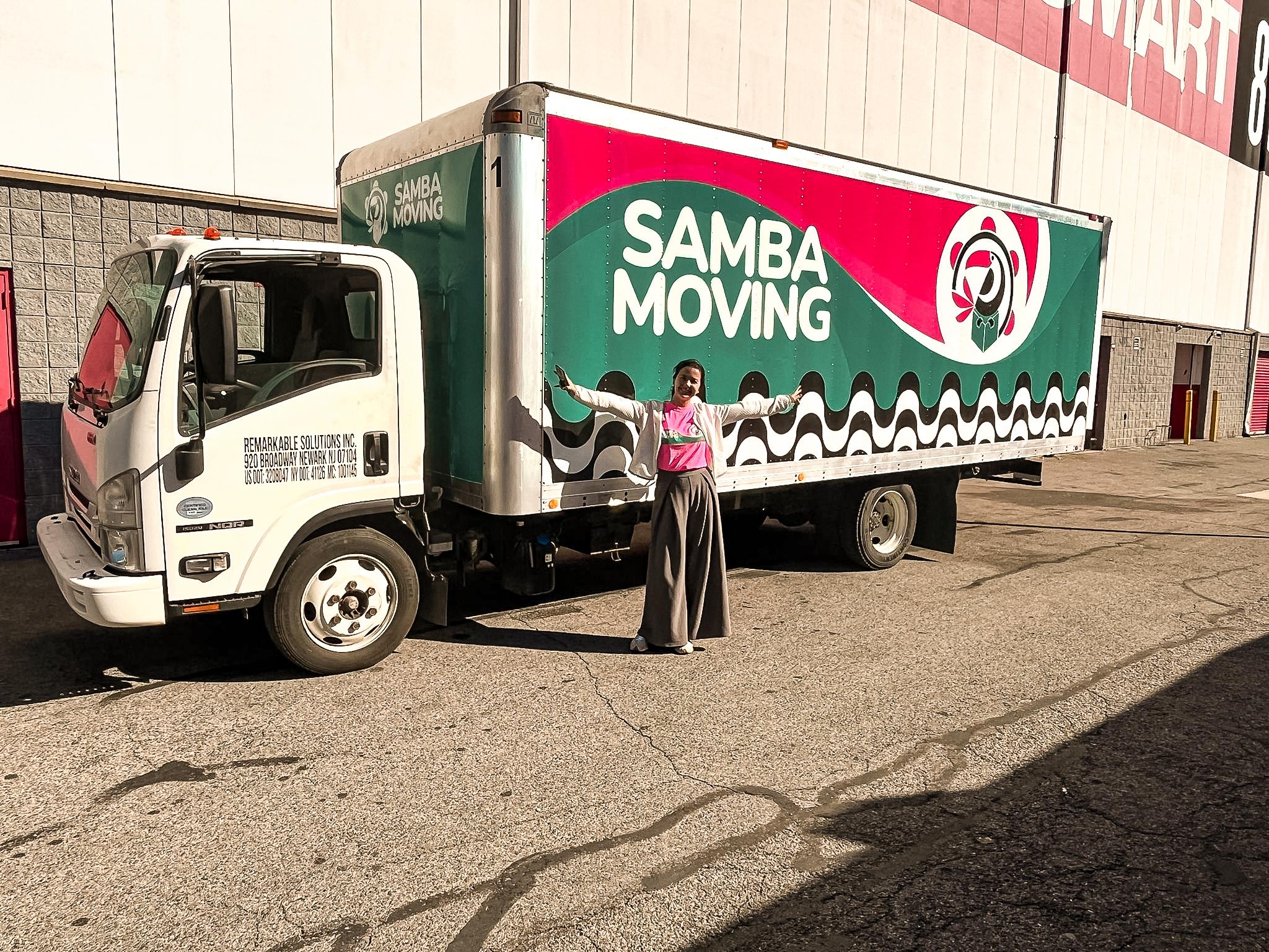 Samba moving truck with woman in front of it.