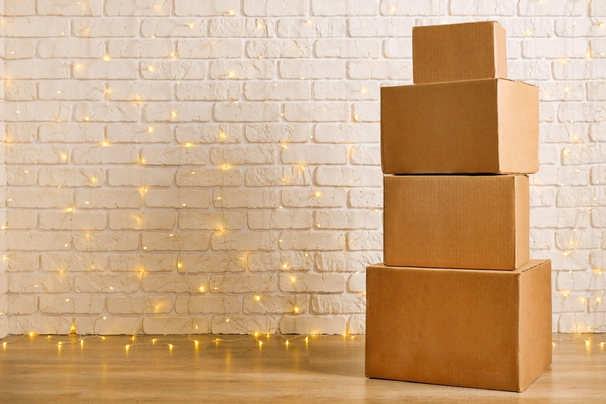 Stack of four blank brown freight boxes, different size, brick wall with Christmas lights on background. Moving company